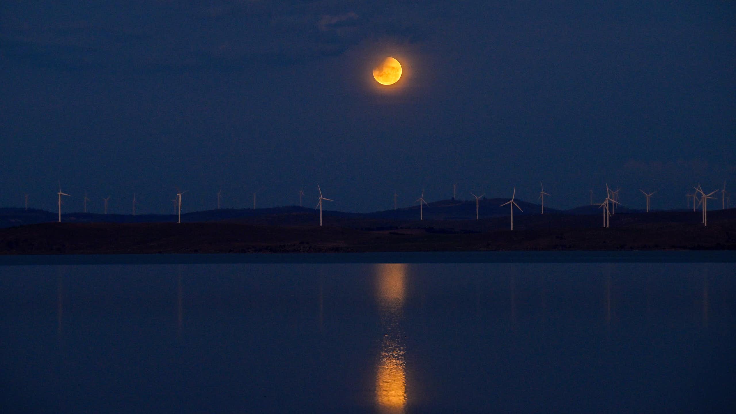 A partially eclipsed orange Moon reflected in the water of a lake