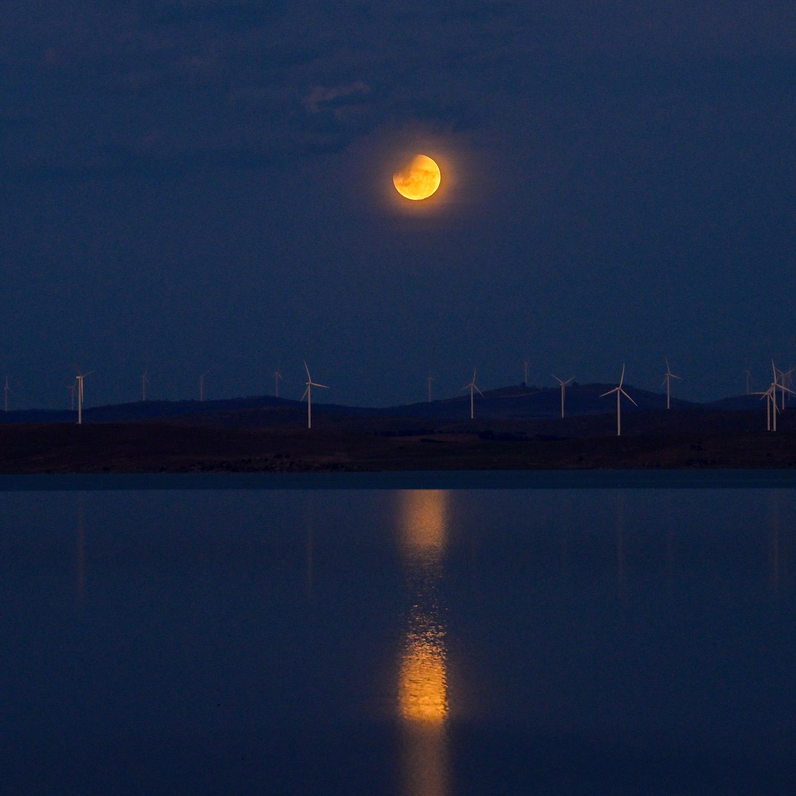 A partially eclipsed orange Moon reflected in the water of a lake