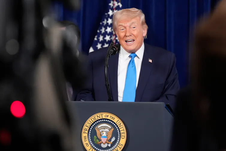 An older white man in a suit speaks from behind a podium