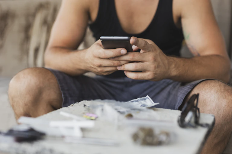 Detail of male drug user''s hands using a smart phone