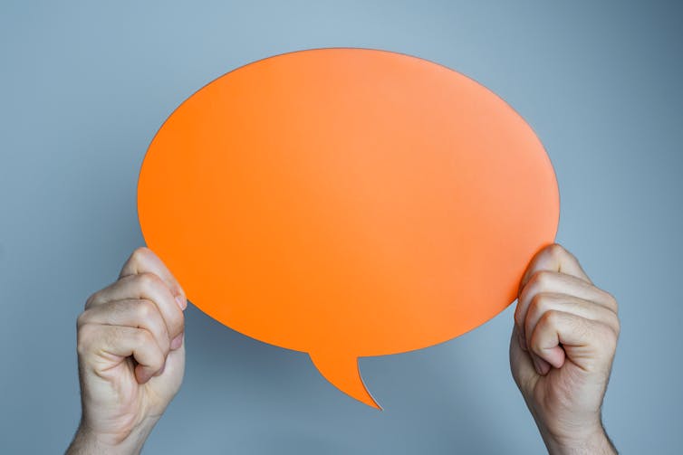 Hands holding blank orange speech bubble on blue background.