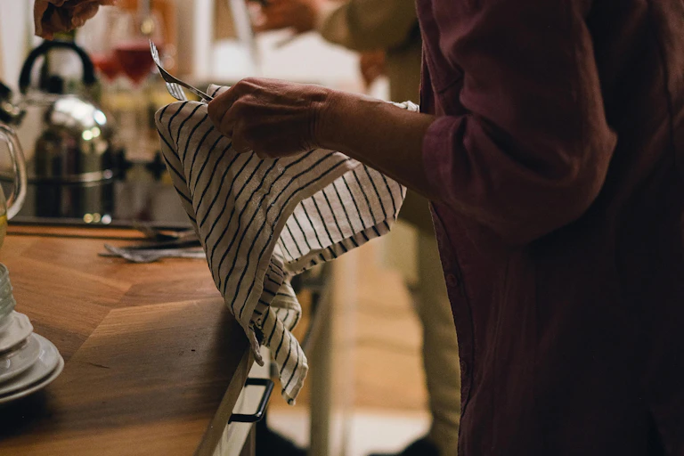 A woman drying forks with a stripey well used dishtowel.
