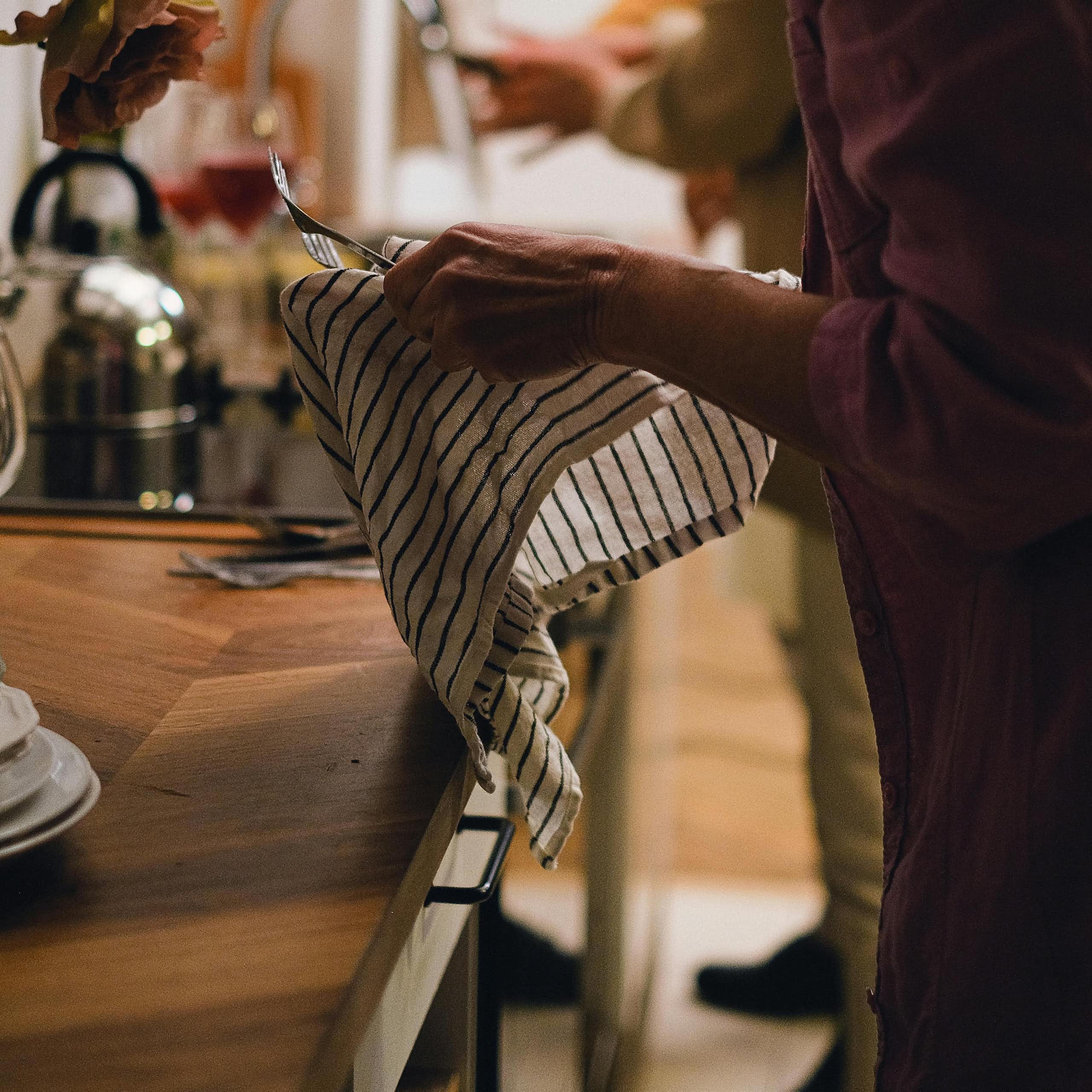 A woman drying forks with a stripey well used dishtowel.