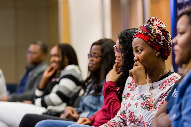 Young people seated in a lecture theatre; one woman looking pensive