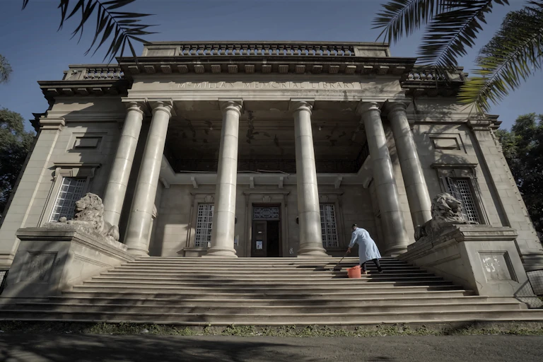 Steps leading up to colonial style building with pillars. A woman is mopping the steps.