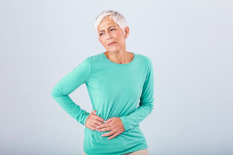 A woman with short white hair holds her hip in pain.