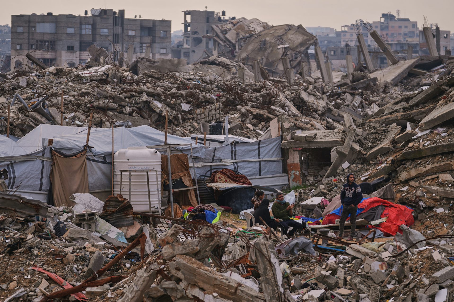 People stand next to a tent set up on top of rubble.