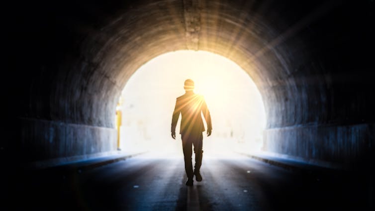 Light at the end of the tunnel 'hope' concept as man walks towards the light