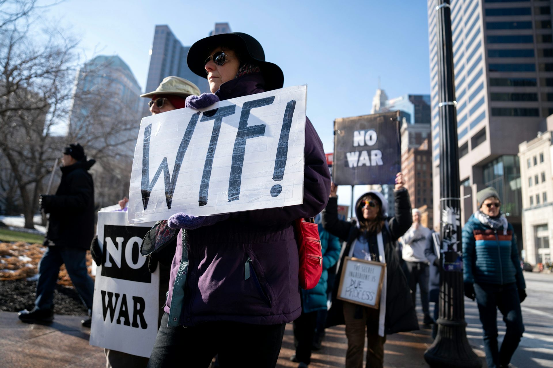 A protester holds a sign that reads WTF. Another person behind him holds a sign that reads No War.