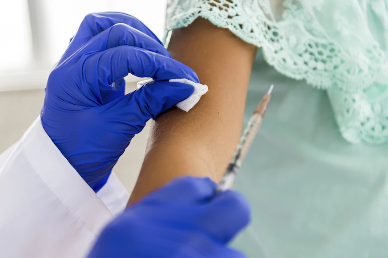 A close-up of a health care worker's gloved hands administering a vaccine into a child's upper arm.