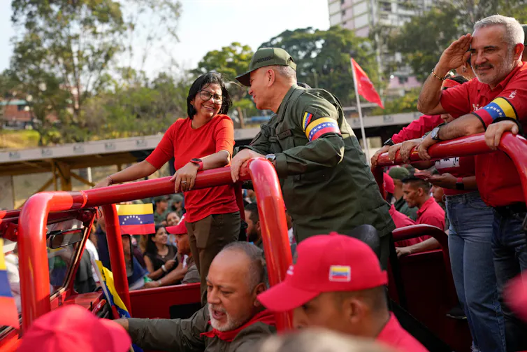 Two political leaders smile at one another as they ride a car during a rally.