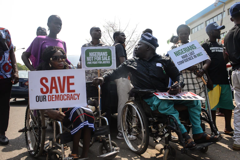Two people in wheelchairs, others standing, holdings posters