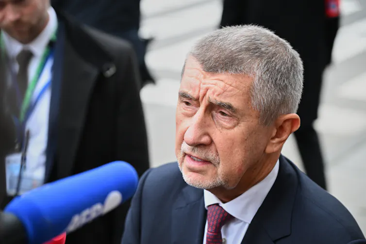 An older man with a short grey buzzcut speaks into a microphone.