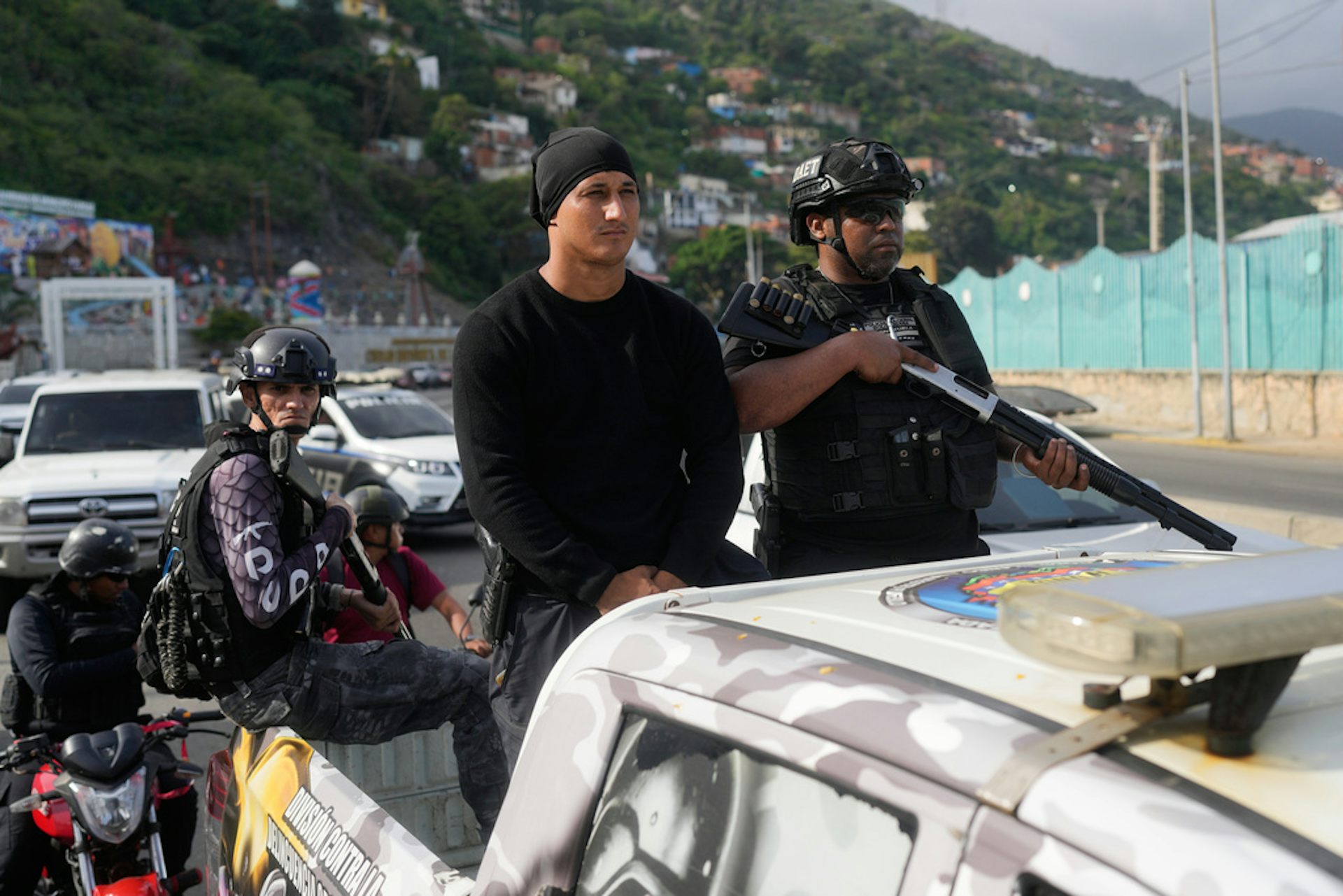 Three armed police officers ride in the back of a pickup truck.