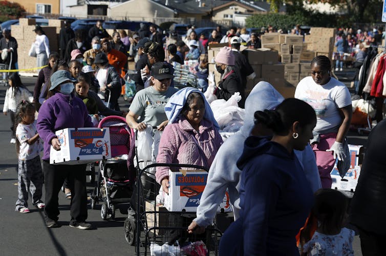 A crowd of people moves through an area with many boxes.