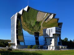 De nombreux miroirs constituant la parabole, face à un bâtiment. On peut voir le reflet du paysage inversé à l’intérieur