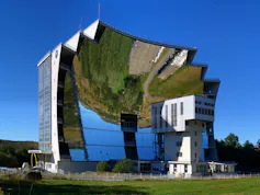 De nombreux miroirs constituant la parabole, face à un bâtiment. On peut voir le reflet du paysage inversé à l’intérieur