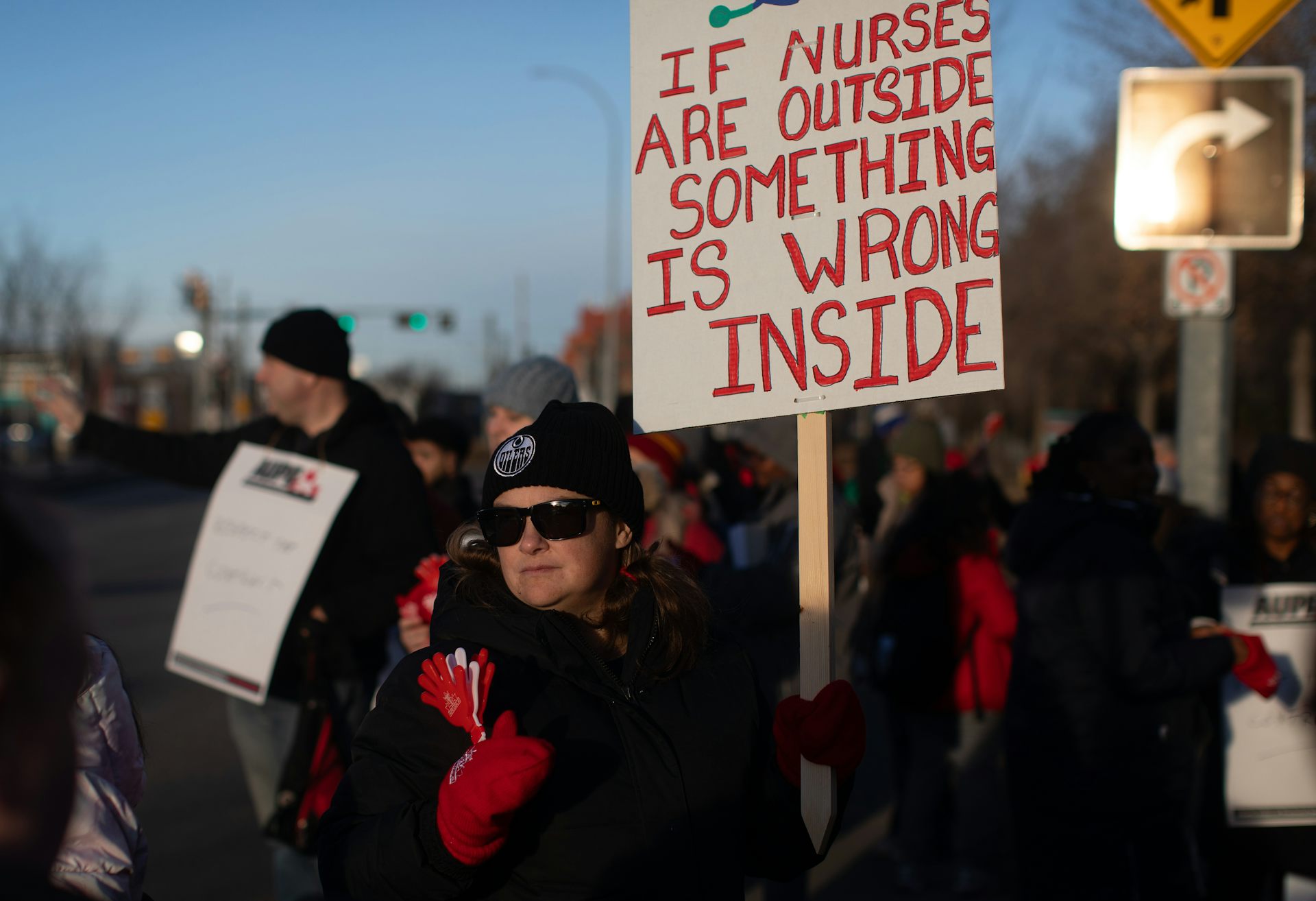 Personas con abrigos y sombreros de invierno sostienen carteles con picas mientras caminan afuera