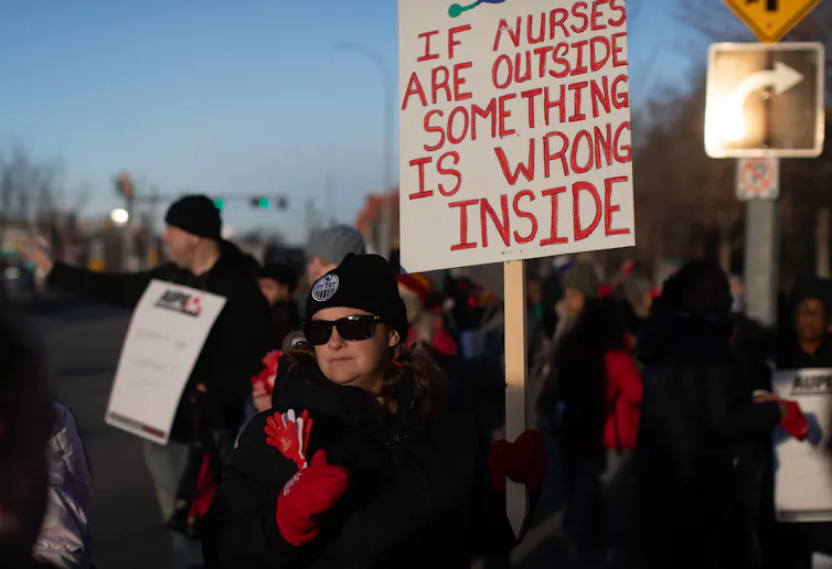 Personas con abrigos y sombreros de invierno sostienen carteles con picas mientras caminan afuera