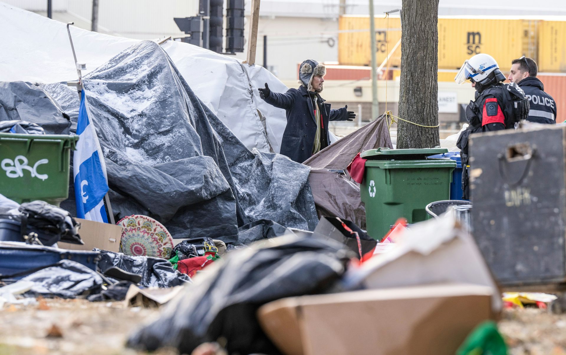 Des policiers discutent avec un itinérant qui lève les bras pour leur bloquer le passage