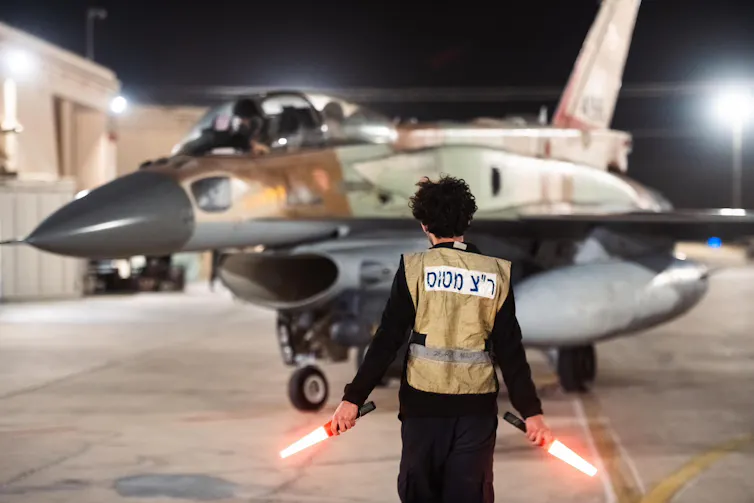A fighter jet taxiing behind a person holding lights.