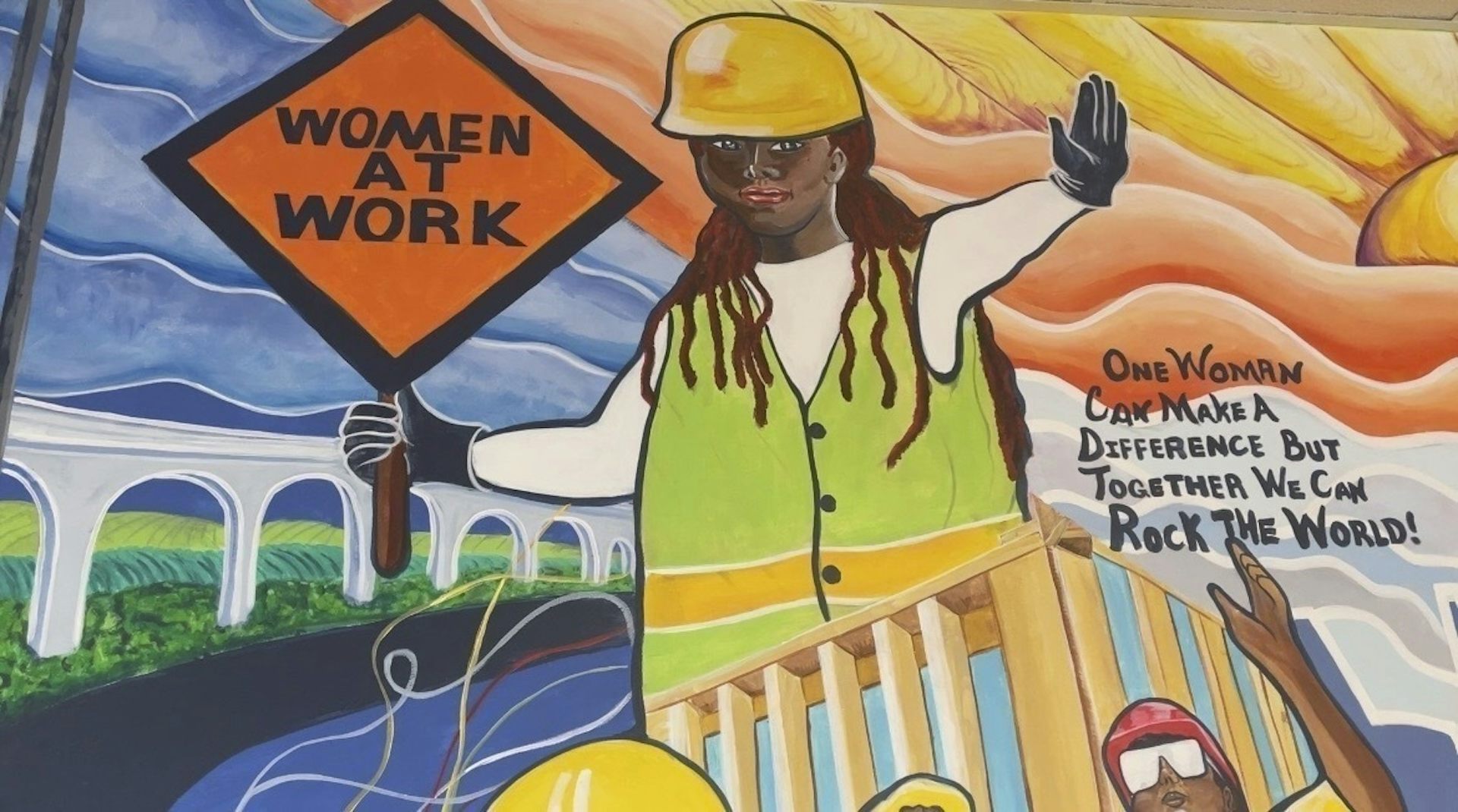 Un mural de una mujer con un casco de construcción sosteniendo un cartel que dice 