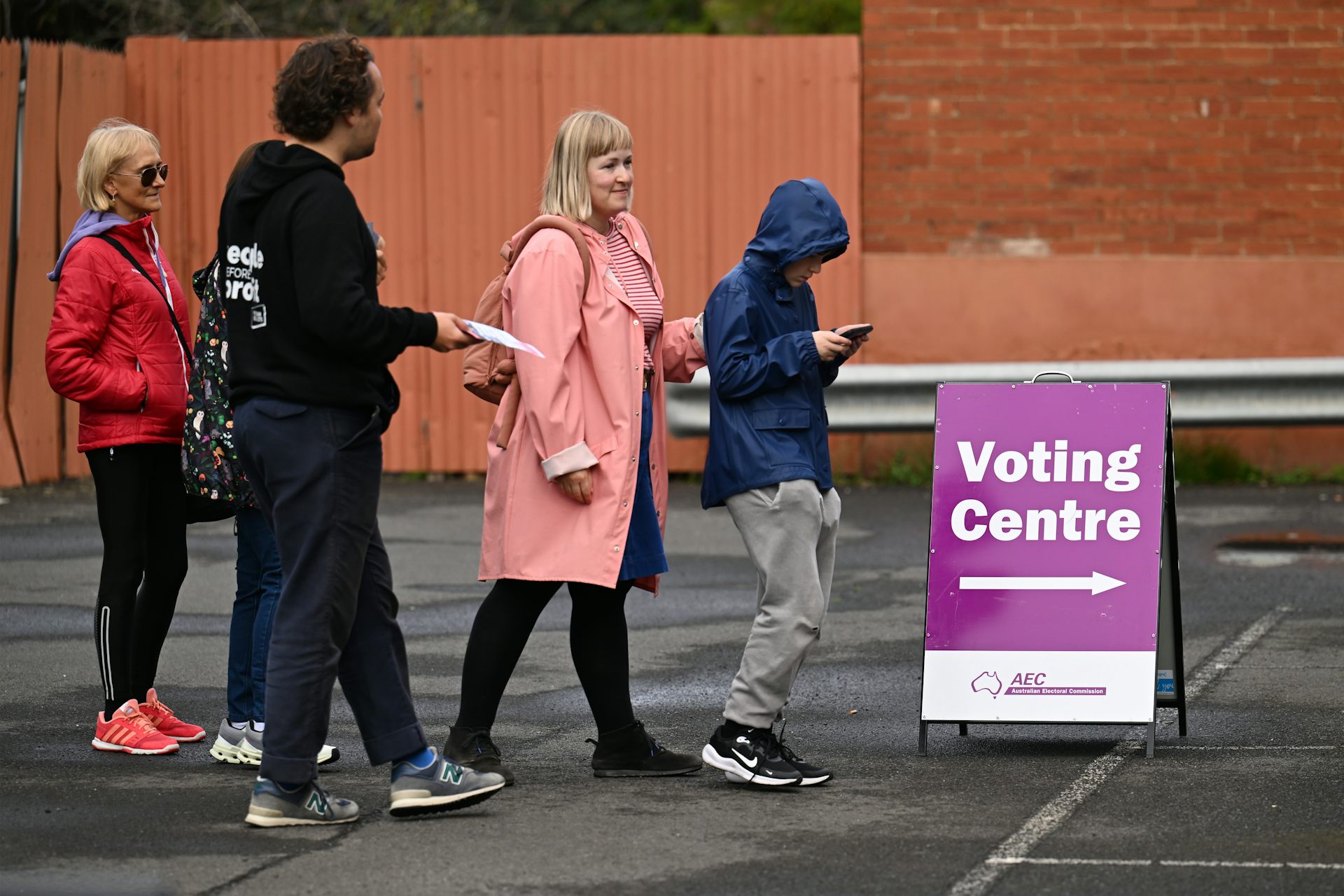 A group of people walking outside next to a sign that says voting centre