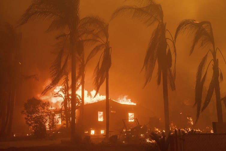 A house behind palm trees burns bright orange in Los Angeles, California.