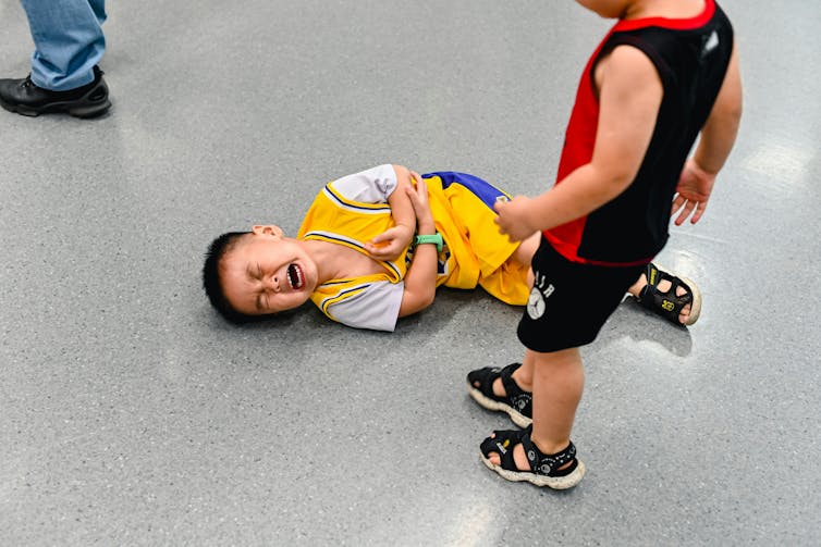 A small boy in sports gear on the ground crying and clutching his elbow.