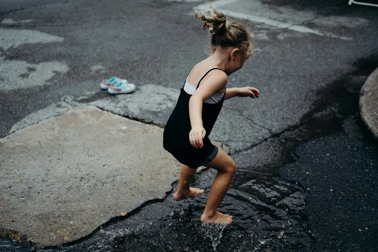 A small girl jumps in a puddle in summer clothing with her shoes off.