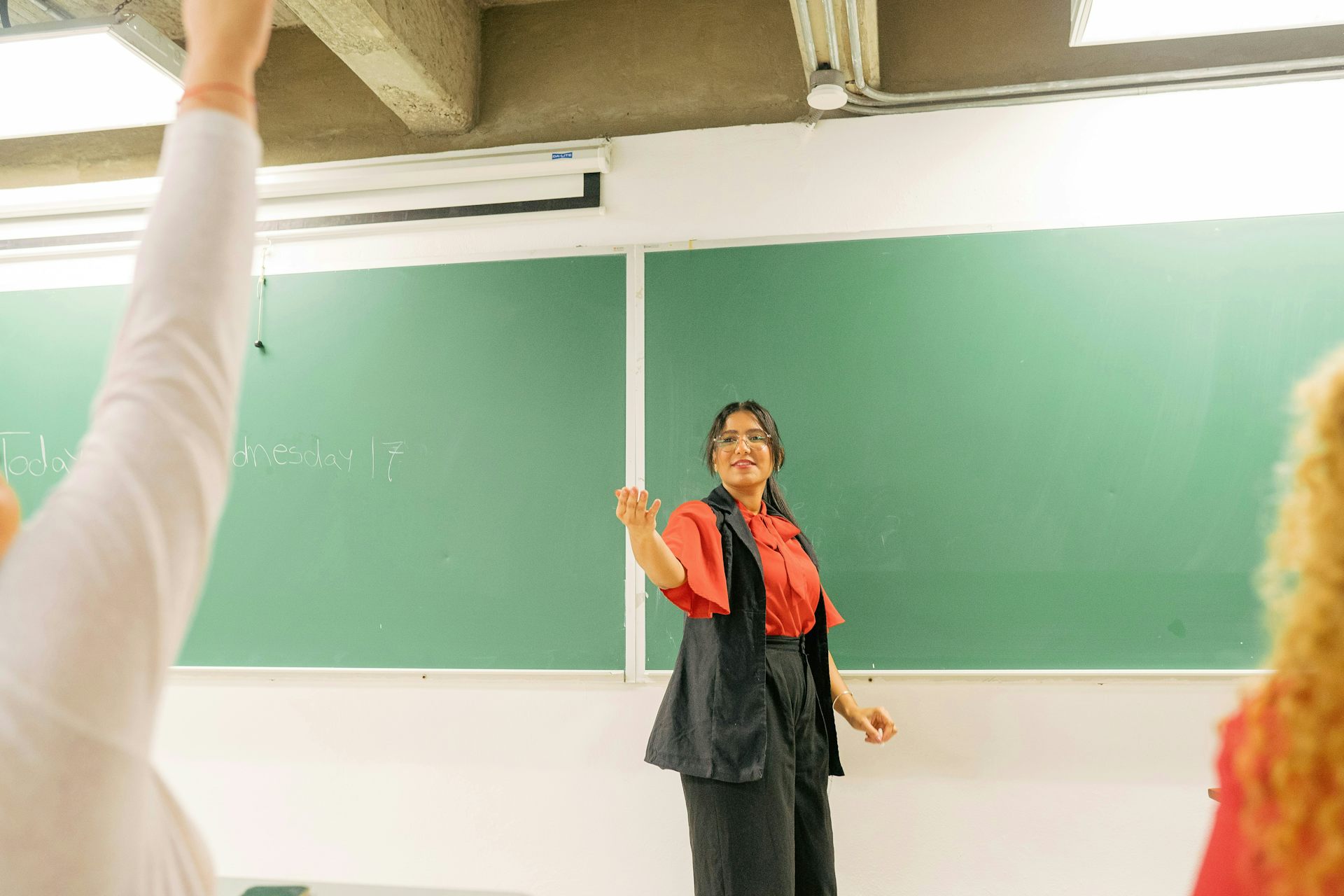 An instructor has their hand extended and speaks as a student hand is seen raised.