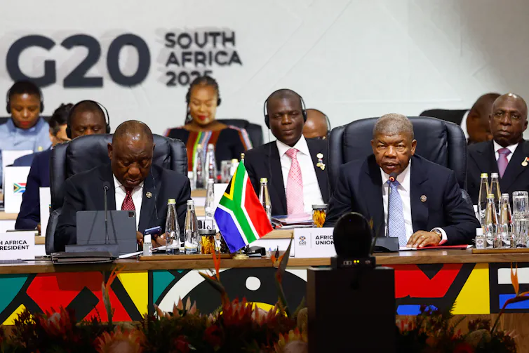 A group of black men in suits sit in front of a G20 banner.