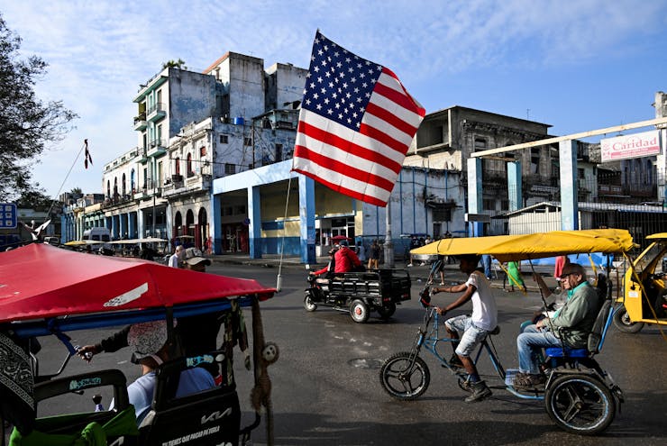 A large US flag is seen flying above street.