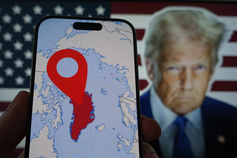 En un móvil se ve un mapa de Groenlandia y el rostro de Trump aparece al fondo.