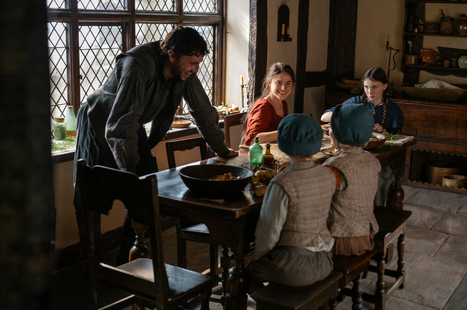 The Shakespeare family in Hamnet sitting round a table smiling
