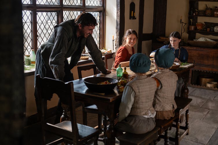 The Shakespeare family in Hamnet sitting round a table smiling
