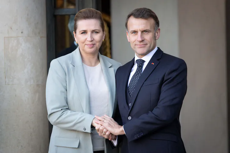 Mette Frederiksen and Emmanuel Macron clasping hands.