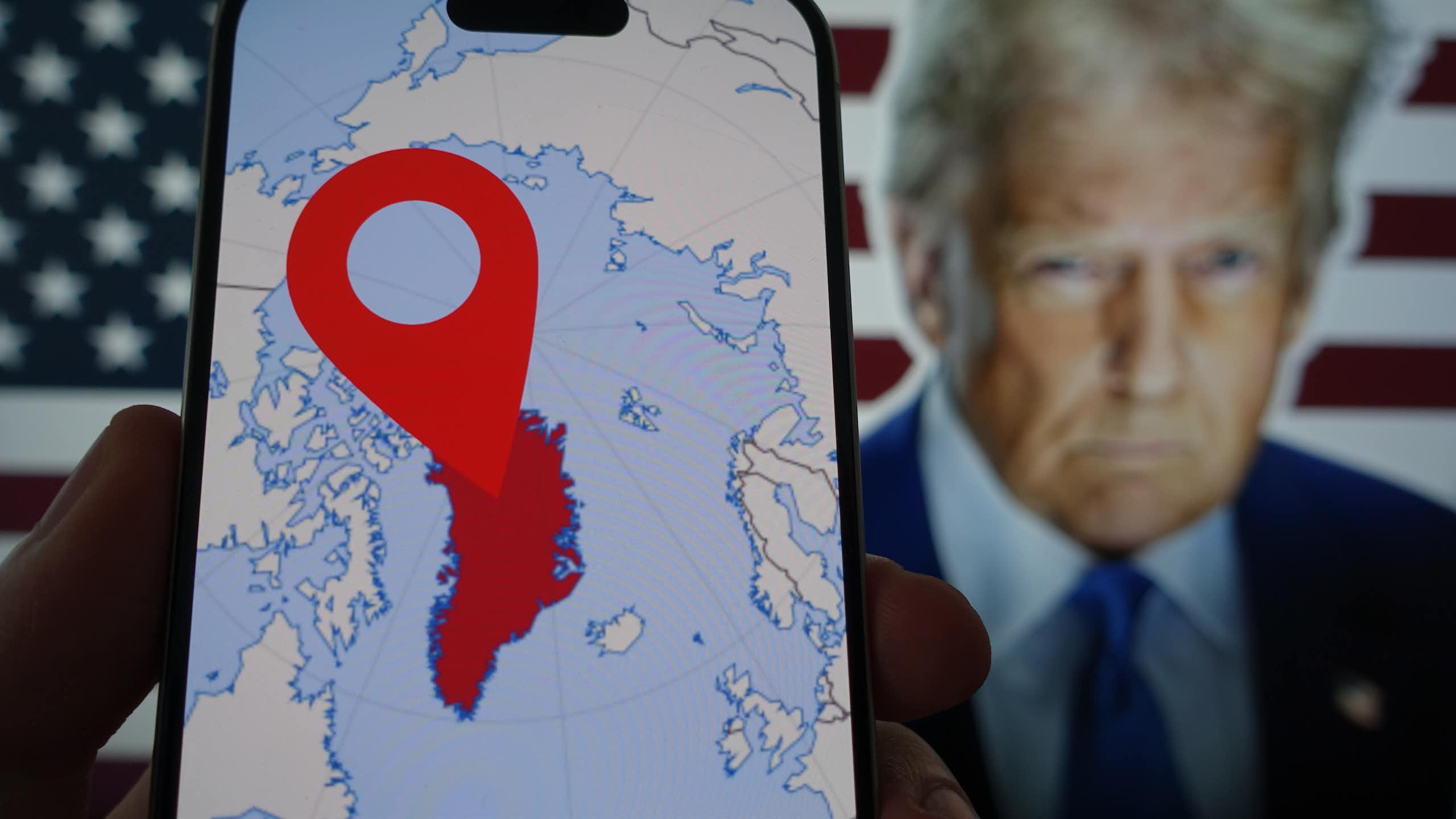 A phone showing a map of Greenland and a picture of Donald Trump in the background.