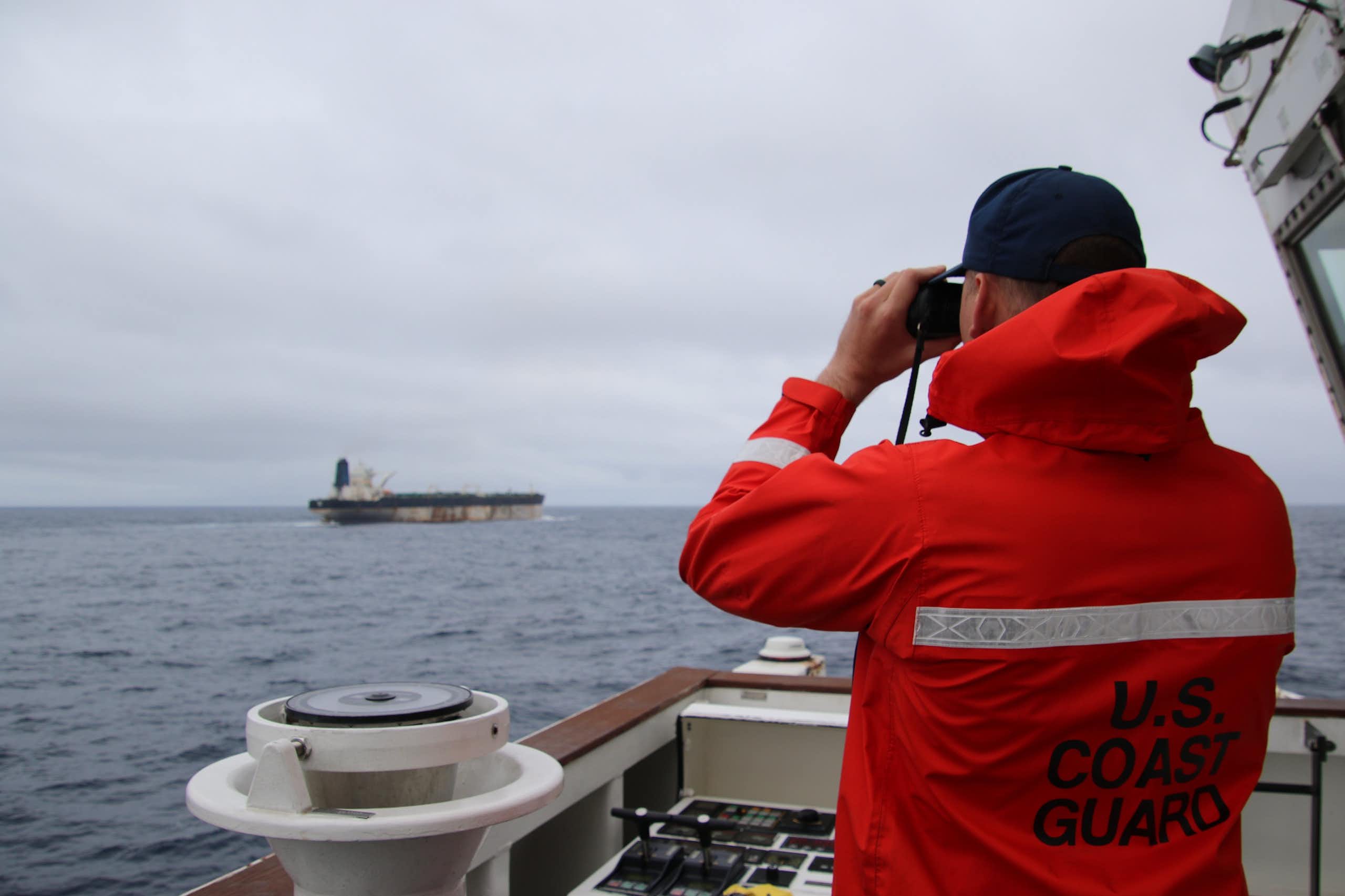 A member of the US Coastguard looks at another vessel through a pair of binolculars.