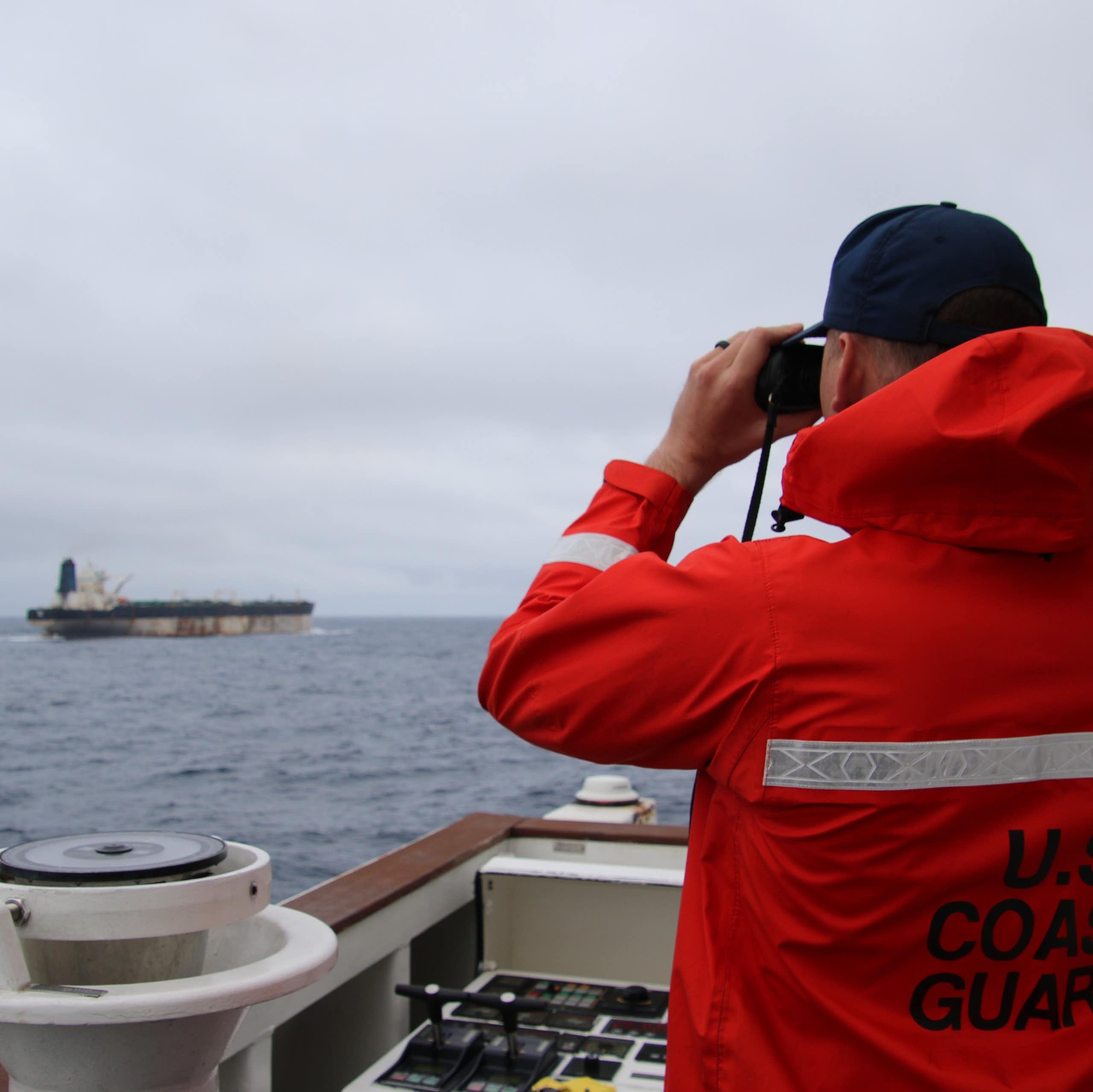 A member of the US Coastguard looks at another vessel through a pair of binolculars.