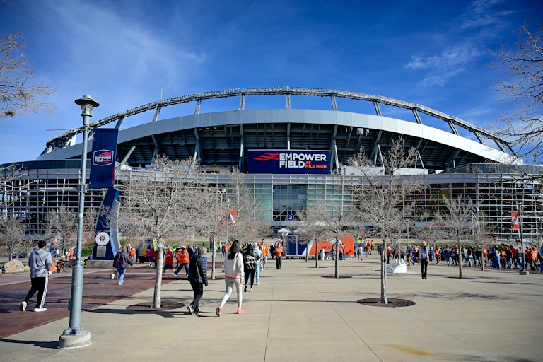 People walk toward a large building with a sign that says "Empower Field at Mile High."