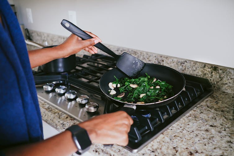 A person stirs vegetables in a frying pan on a gas stove.