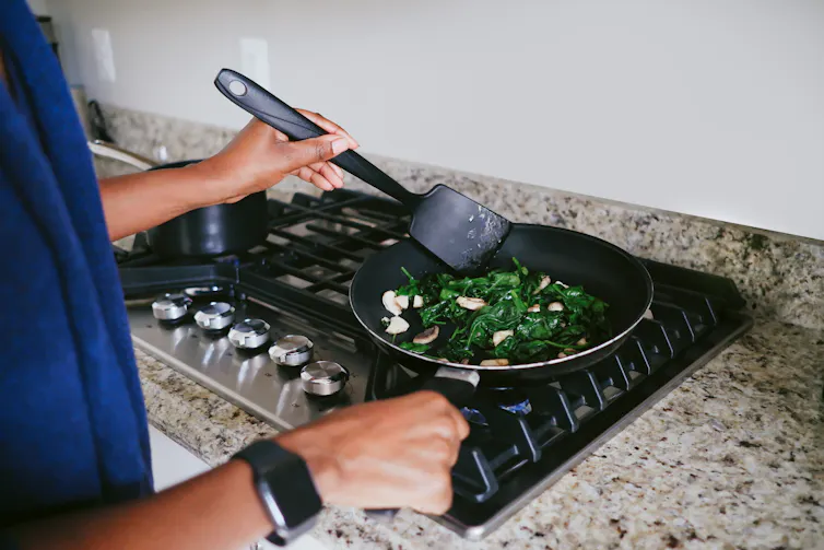 A person stirs vegetables in a frying pan on a gas stove.