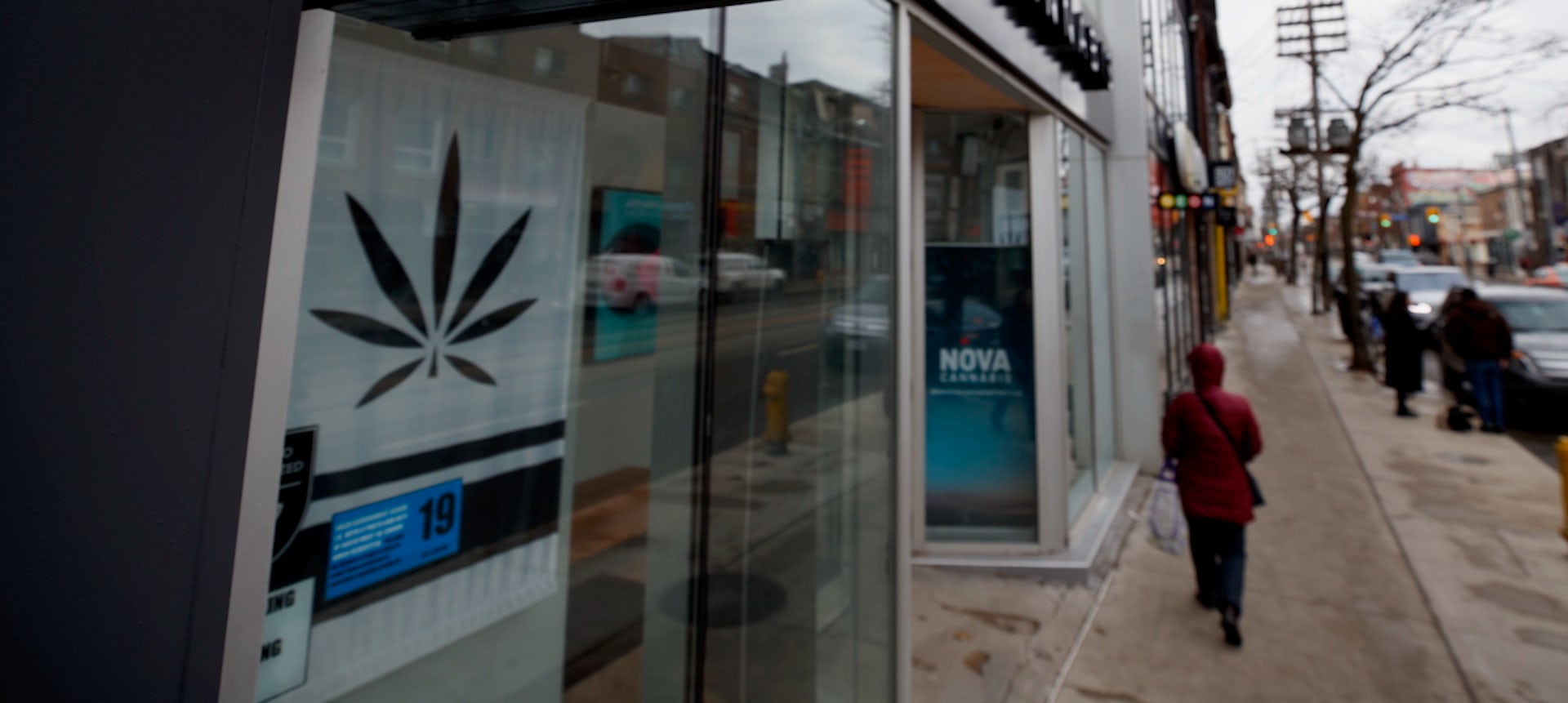 Una mujer vista desde atrás pasando por una tienda de cannabis.