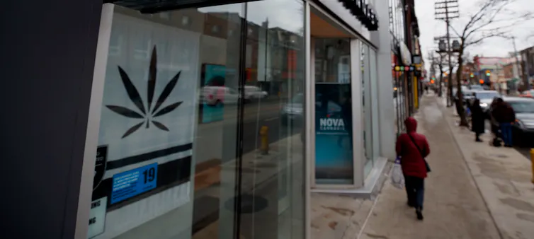 A woman seen from behind walking past a cannabis store