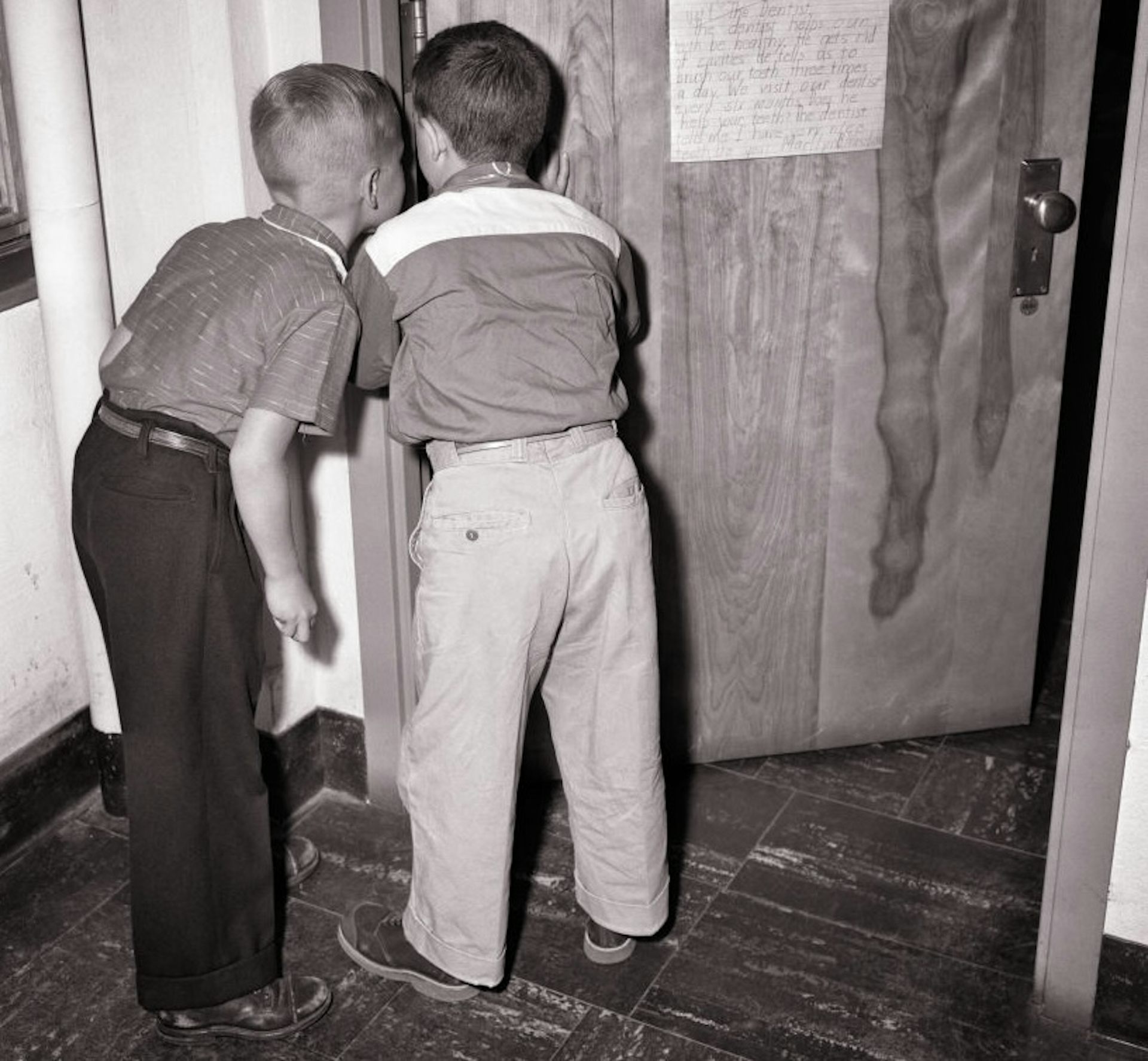 Vintage photograph of two young boys peering through a crack in a door.