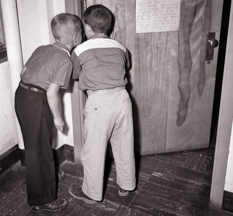 Vintage photograph of two young boys peering through a crack in a door.