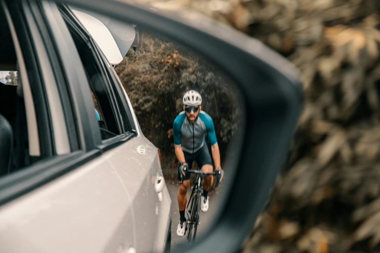 A man on a bike is reflected in a car side mirror.