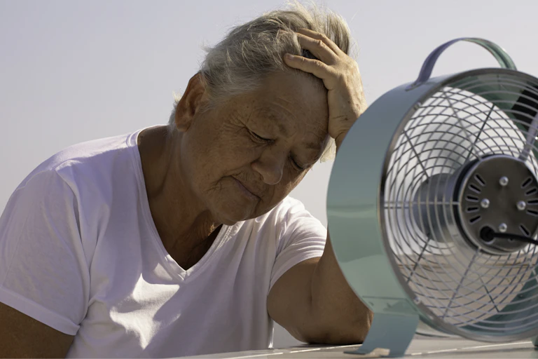Older woman with eyes closed faces a fan.
