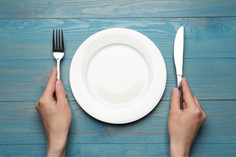 Empty plate surrounded by hands holding a fork and a knife
